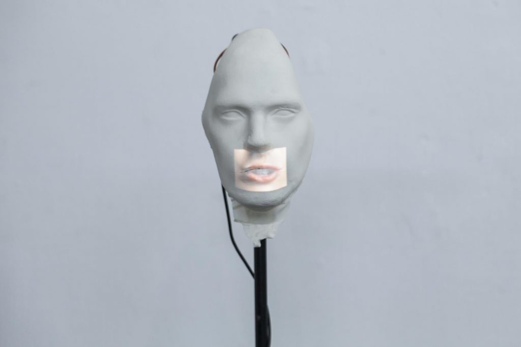 “Vedetes”, 2017, máscara de látex, pedestal de microfone, ferro, servomotor, arduino, projetor, dimensões variáveis

